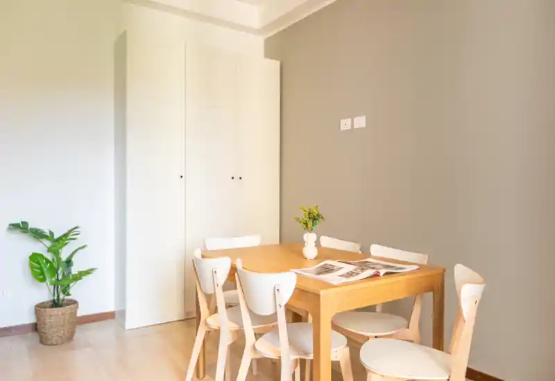 Coin repas lumineux et minimaliste avec une table en bois, six chaises blanc/massif et un petit vase au centre — cadre moderne et chaleureux pour de petits repas.