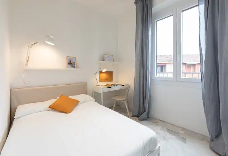 Bright, well-styled bedroom with a comfortable double bed, bedside lamps and a small desk by the window — ideal for rest and light work.