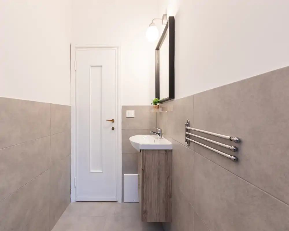 Bagno moderno e luminoso con lavabo sospeso, specchio con anta e scaldasalviette, rivestimenti in piastrelle grigie neutre.