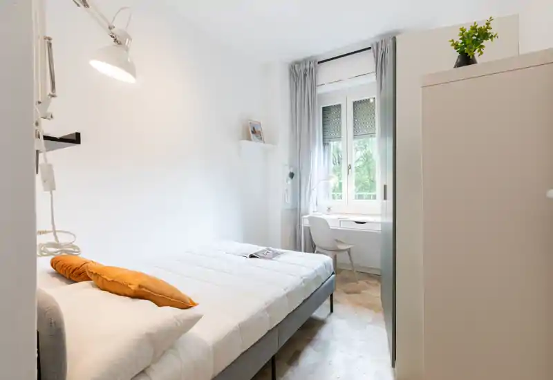 Dormitorio luminoso y compacto con cama doble, ropa de cama suave, escritorio junto a la ventana y armario — ideal para una persona o pareja que busca un espacio limpio y minimalista.