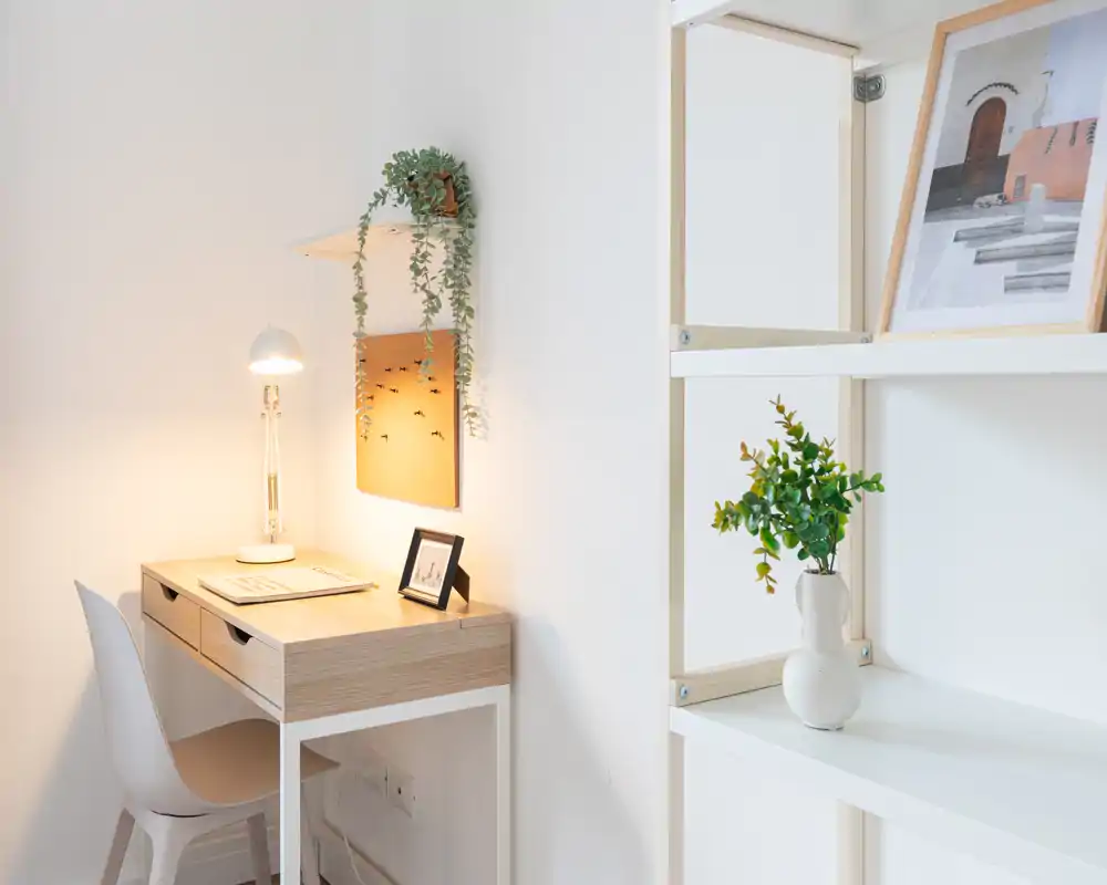 Rincón de oficina en casa luminoso y minimalista con escritorio de madera, lámpara y plantas decorativas: un espacio acogedor y bien iluminado para trabajar.