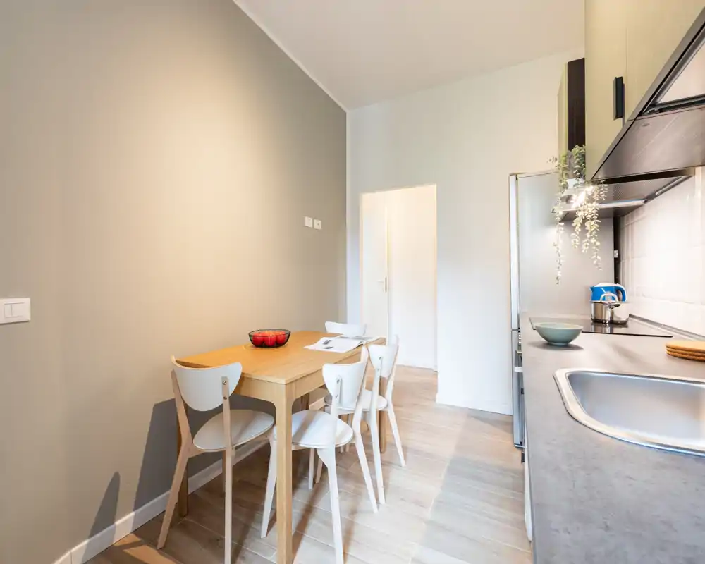 Área de comedor luminoso y moderno con mesa de madera para cuatro y una encimera elegante con fregadero, ideal para comidas informales en un espacio abierto compacto.