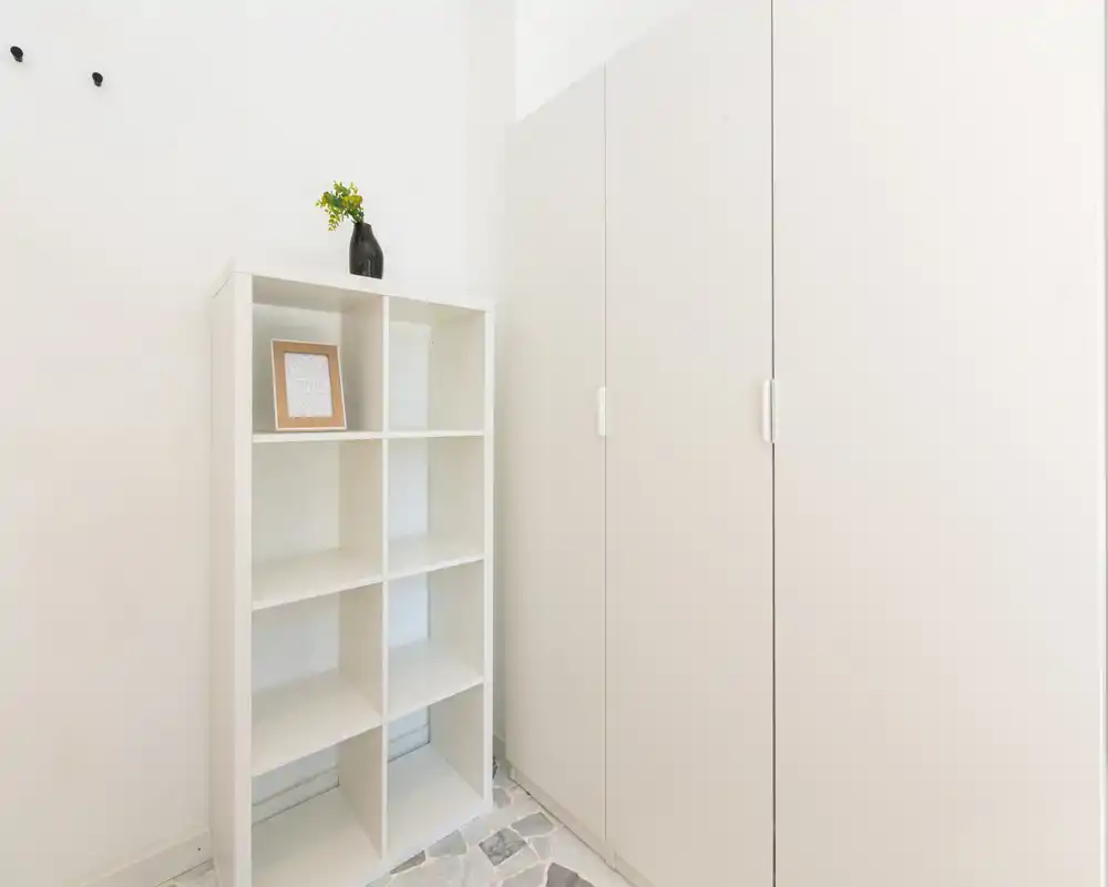 Pequeño recibidor luminoso con armario empotrado y estantería abierta; estilo minimalista y suelo de baldosas, ideal para abrigos y zapatos.