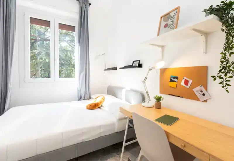 Dormitorio moderno y luminoso con cama doble bien hecha, escritorio de madera y ventana con vistas a la vegetación — ideal para trabajar o relajarse.