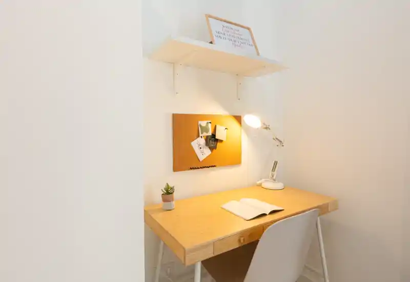 Rincón de estudio luminoso y minimalista con escritorio de madera, lámpara de trabajo, panel de corcho y pequeña planta — ideal para trabajar o leer en un espacio compacto.