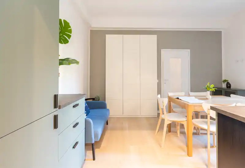 Zona de estar/comedor luminosa y amplia con sofá azul compacto, mesa de madera y mobiliario moderno — ideal para un apartamento urbano y acogedor.