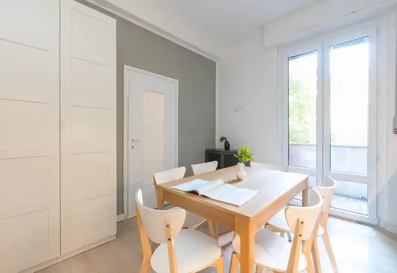 Área de comedor moderna y luminosa con mesa de madera y seis sillas junto a grandes puertas de cristal que dan a una pequeña terraza; decoración minimalista y ambiente aireado.