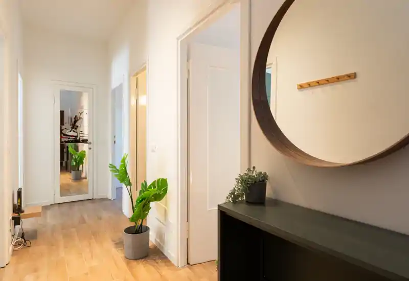 Vestíbulo/pasillo luminoso con suelo de madera, espejo redondo decorativo y plantas — un espacio de entrada acogedor.