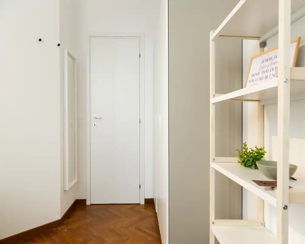 Minimal, well-lit entrance hallway with parquet flooring, a wall mirror and open shelving — clean and welcoming first impression.