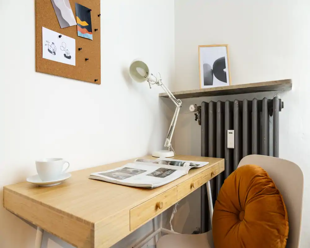 Bright, styled corner desk with a wooden tabletop, task lamp, magazine and a cozy chair with an orange cushion — ideal for remote work or reading.
