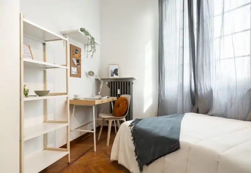Bright, cozy bedroom with a neatly made bed, soft throw and a compact desk by the window — ideal for rest and study.