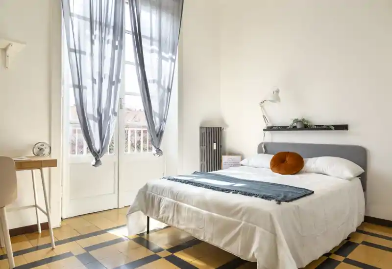 Bright, airy bedroom with a comfortable double bed, soft textiles and natural light from French doors — ideal for relaxing stays.