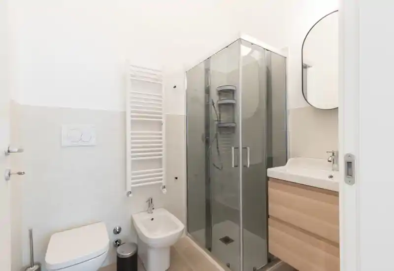 Modern, compact bathroom with a glass shower enclosure, wall-mounted toilet, bidet and a wooden vanity with sink. Bright, clean styling suitable for rental listings.