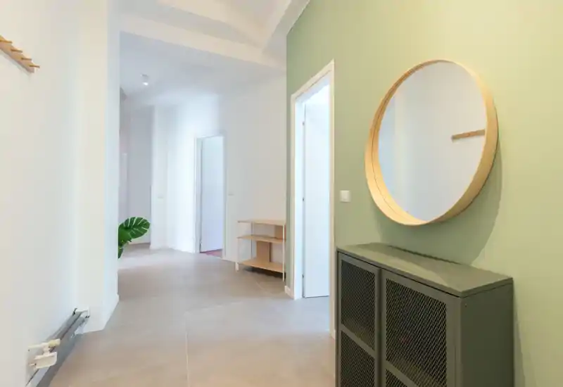 Bright, minimal entrance hallway with tiled floor, round wall mirror and compact storage cabinet — a welcoming arrival space.