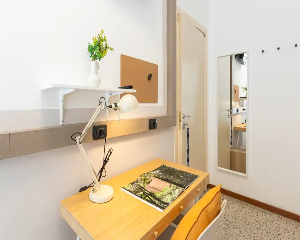 Espacio de trabajo compacto y luminoso con escritorio de madera, lámpara articulada, corcho y espejo — ideal para concentrarse en un apartamento pequeño.