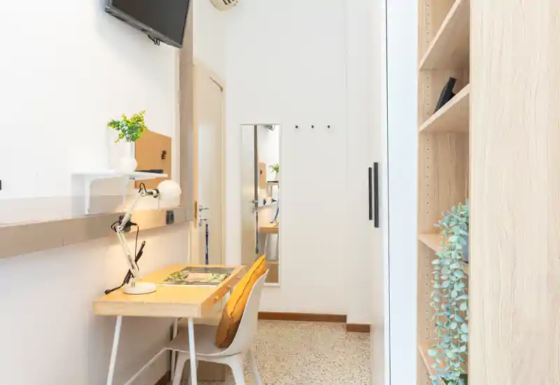 Rincón de oficina en casa luminoso y compacto con escritorio de madera, lámpara de tarea y planta decorativa — moderno y apto para trabajo concentrado.