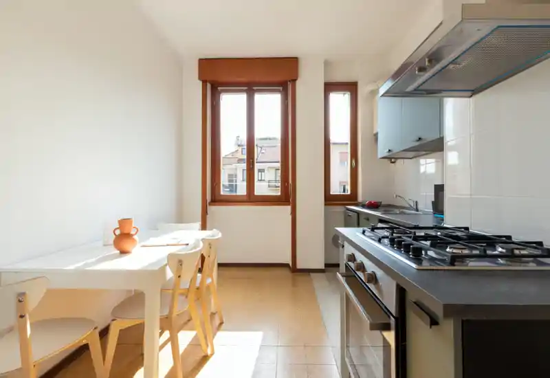 Cocina luminosa y compacta con mesa para cuatro, cocina de gas y mucha luz natural por las ventanas — ideal para comidas informales.