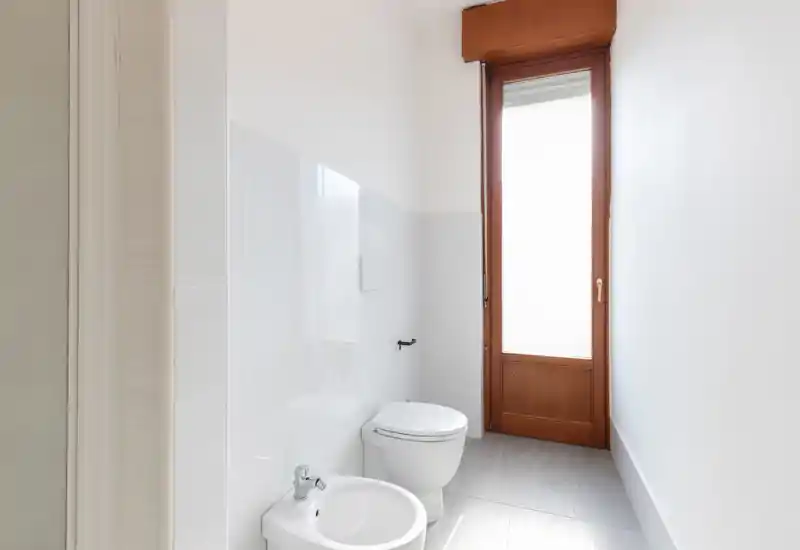 Pequeño baño moderno con inodoro y bidé, media pared alicatada y una ventana alta que proporciona suave luz natural.