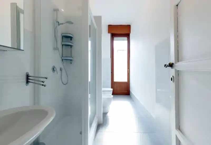Baño moderno y luminoso con ducha con mampara de vidrio, sanitarios y una gran ventana que aporta luz natural.