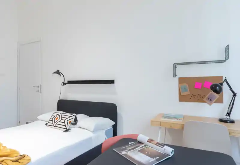 Bright, modern bedroom with a neatly made double bed, bedside lamp and a small desk area — clean minimalist styling ideal for rental listings.