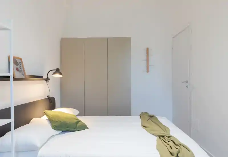 Bright, minimalist bedroom with a large bed, neutral wardrobe and green accent textiles for a calm, modern feel.