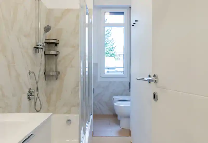 Bright, modern bathroom with a shower-tub combo, wall-mounted shower fixtures and a toilet next to a frosted window.