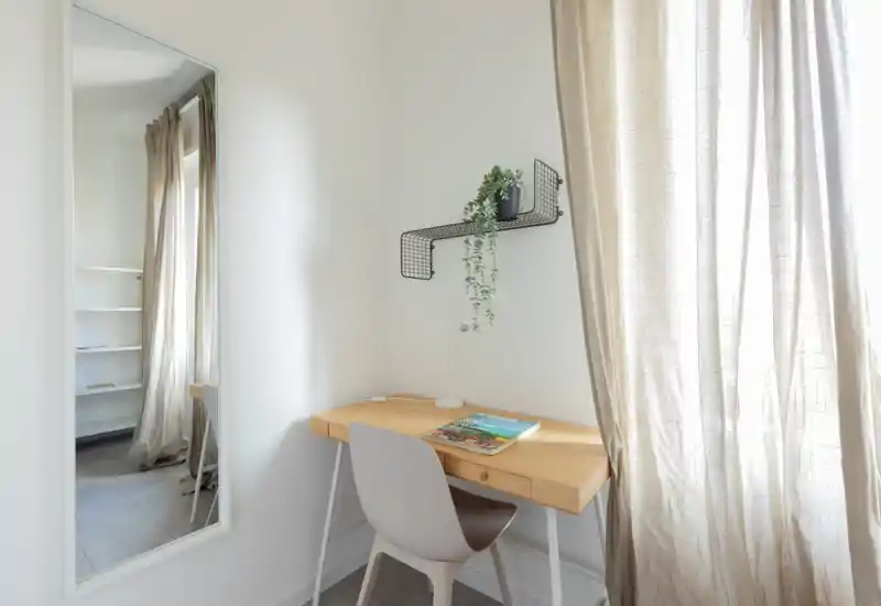 Bright, minimalist corner desk with a wooden tabletop, chair and a decorative hanging shelf — ideal as a study nook in the bedroom.