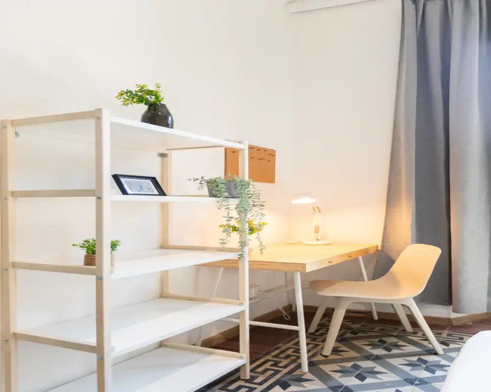 Spazio di lavoro luminoso e minimal con scrivania in legno, sedia moderna, scaffale e piante decorative — perfetto per smart working o studio.
