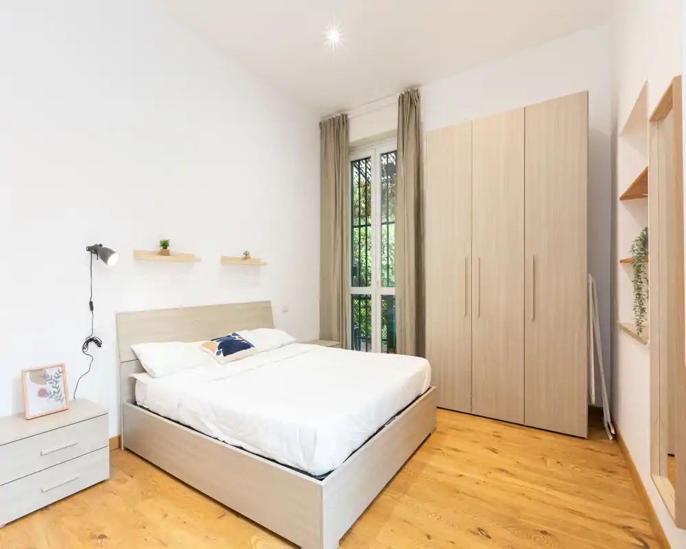 Bright, modern bedroom with a double bed, wooden floor and a large wardrobe; neutral tones and simple decor create a calm, airy atmosphere.