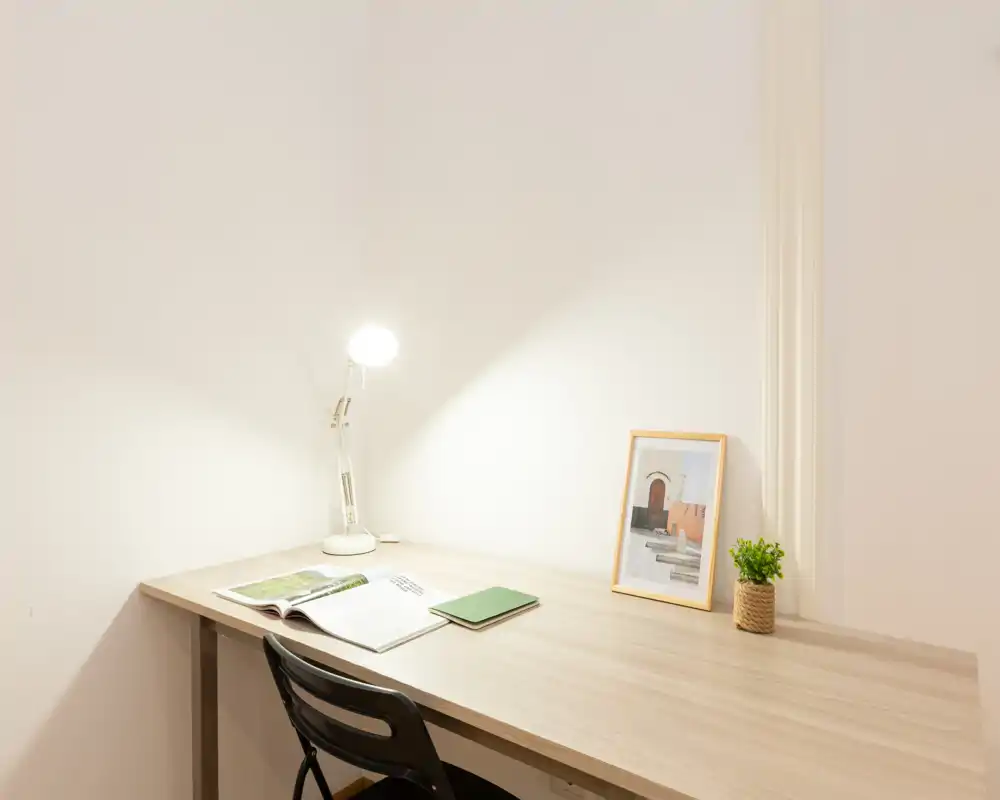 A bright, minimalist work corner with a wooden desk, desk lamp, small plant and framed photo — ideal for a compact home office or study nook.