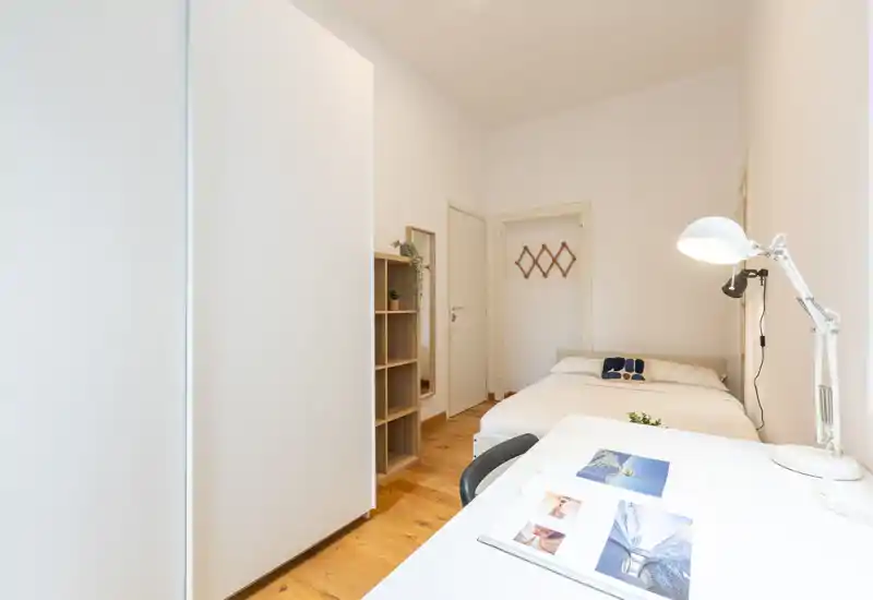 Bright, minimalist bedroom with a double bed, desk and wardrobe. Clean lines, wooden floor and neutral decor create a calm, functional space ideal for short-term rentals.