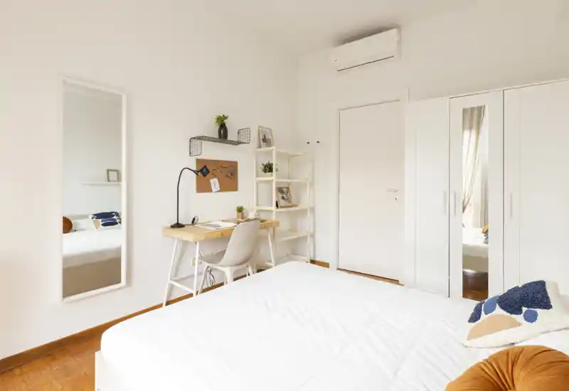 Camera da letto luminosa e minimalista con un comodo letto matrimoniale, un armadio con ante a specchio e una scrivania ideale per lavoro o studio.