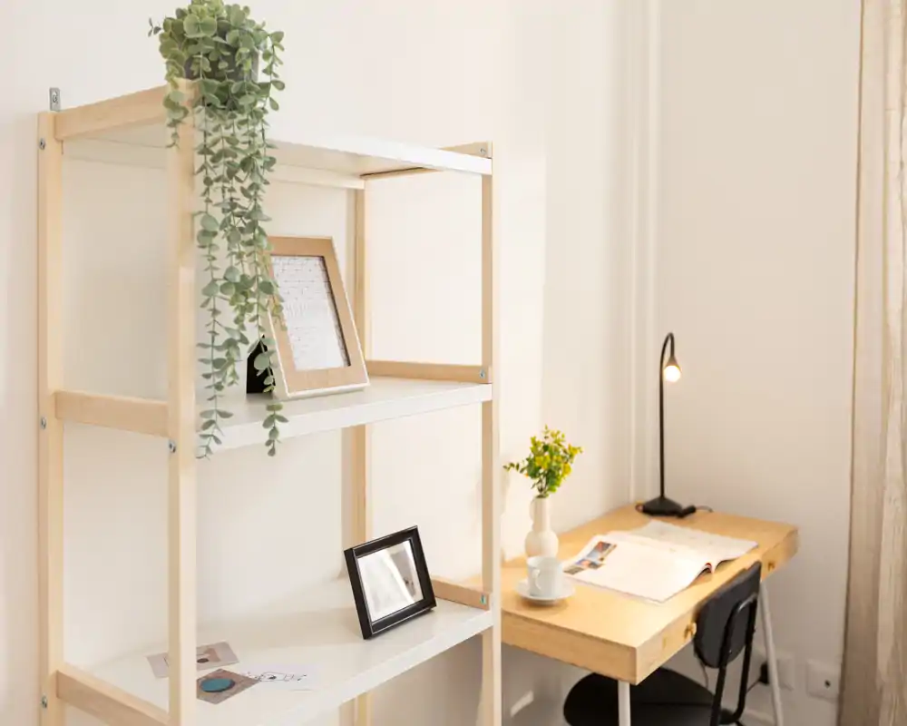 Angolo camera luminoso e minimale con scrivania in legno, lampada da tavolo e scaffale con piante e cornici; perfetto come area di lavoro tranquilla nella stanza da letto.
