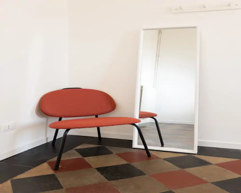 Angolo d'ingresso minimale con una panca moderna per due, specchio appoggiato e pavimento piastrellato a motivi — stile pulito e semplice ideale per un ingresso d'appartamento.