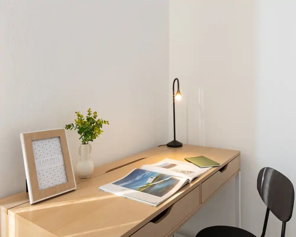 Angolo lavoro luminoso e minimal con scrivania in legno, piccola lampada, rivista aperta e decorazioni semplici per un’atmosfera calma.