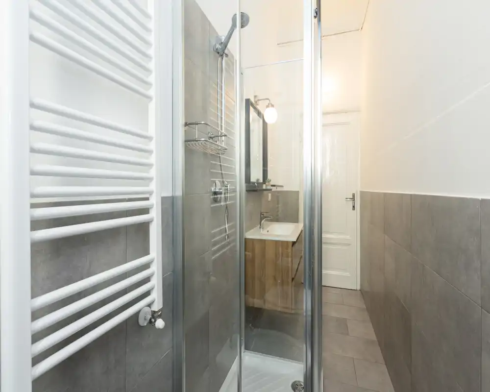 Bagno moderno e luminoso con cabina doccia in vetro, scaldasalviette a parete e lavabo compatto con mobiletto in legno.