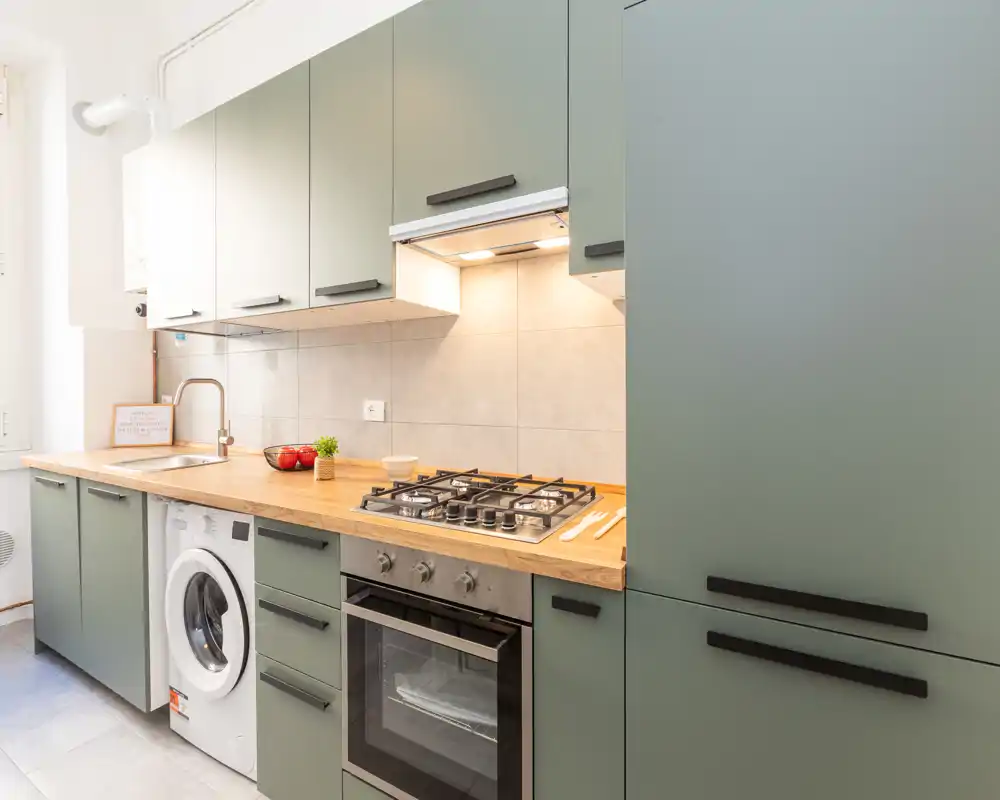 Cucina moderna e luminosa con mobili verdi, piano in legno, forno ad incasso e piano cottura a gas, oltre a lavatrice integrata — compatta e ben organizzata.