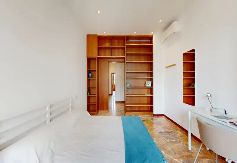 Bright, modern bedroom with a white bed, teal runner and built-in wooden shelving creating a clean, airy feel.