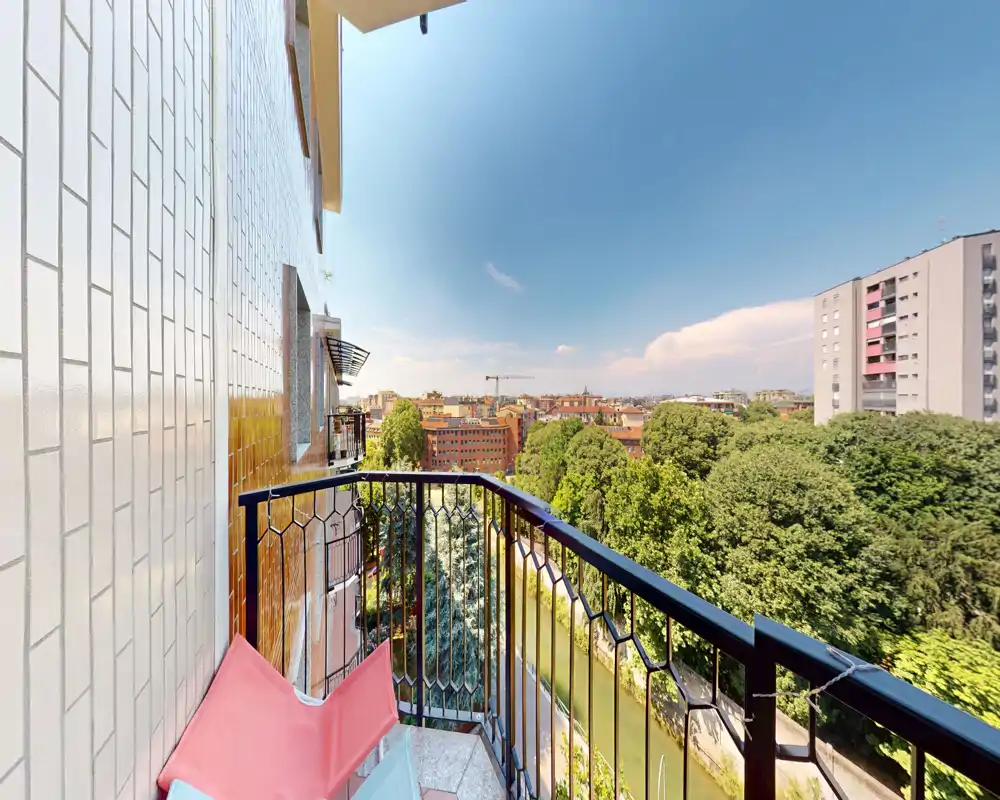 Balcón privado soleado con barandilla de metal y vistas a la ciudad entre copas de árboles — ideal para relajarse al aire libre.