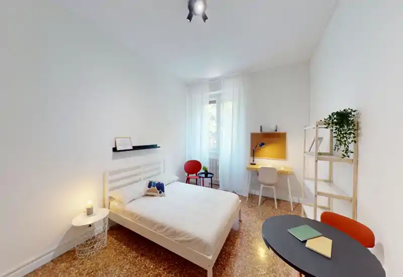 Bright, modern bedroom with a white double bed, bedside table and a small workspace by the window. Neutral décor, terrazzo floor and soft natural light make it ideal for a comfortable stay.