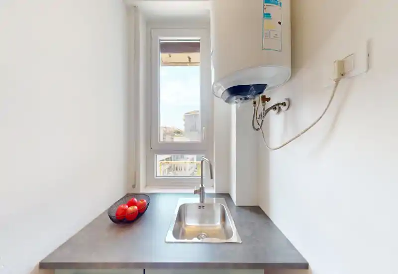 Compact kitchenette with a stainless steel sink, faucet and a window providing natural light; a small fruit bowl adds a touch of color.