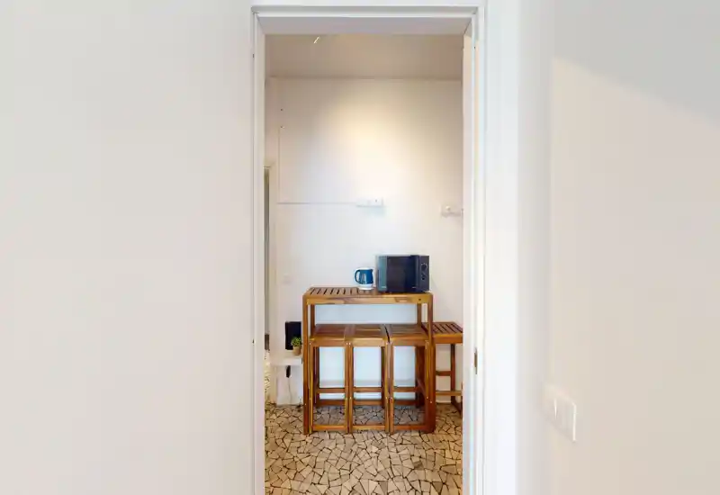 Compact kitchenette area seen through a doorway with a wooden counter, stools and small appliances; simple, functional space ideal for light meals.
