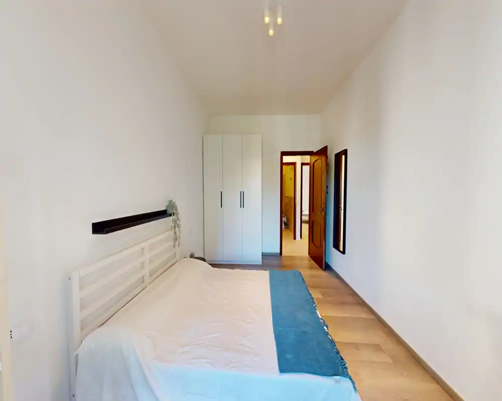 Chambre claire et minimaliste avec lit double, tête de lit blanche et plaid bleu ; armoire et porte visibles, idéale pour une annonce locative.