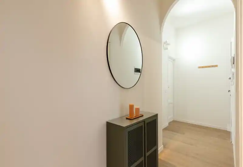 Ingresso luminoso e minimale con specchio rotondo a parete, mobile consolle sottile e pavimento in legno — un'entrata accogliente dal design moderno e pulito.