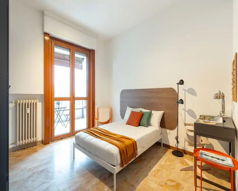 Dormitorio luminoso y bien decorado con cama doble, cabecero de madera y gran puerta de cristal que da a un pequeño balcón. Textiles suaves y cojines decorativos crean un ambiente acogedor y moderno, perfecto para anuncios.