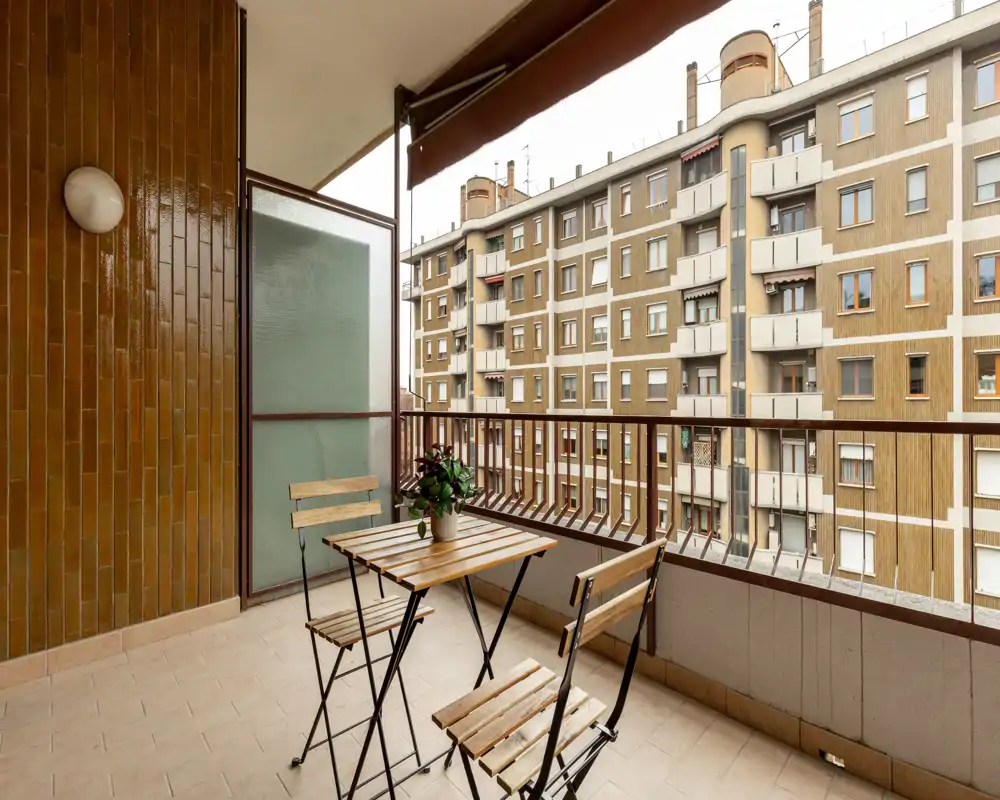 Balcón soleado con una pequeña mesa de madera y tres sillas plegables, con vistas a los edificios vecinos — ideal para el café de la mañana.