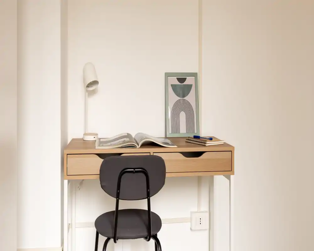 Spazio di lavoro luminoso e minimale con scrivania in legno, lampada da tavolo, stampa incorniciata e sedia semplice — ideale per studio o lavoro da remoto.
