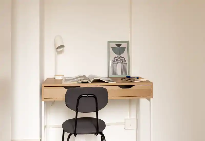 Spazio di lavoro luminoso e minimale con scrivania in legno, lampada da tavolo, stampa incorniciata e sedia semplice — ideale per studio o lavoro da remoto.