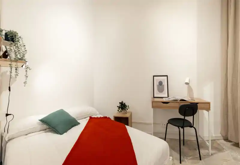 Camera da letto luminosa e minimal con letto bianco, plaid rosso e una scrivania compatta sulla parete — linee pulite e luce soffusa per un'atmosfera moderna e rilassante.