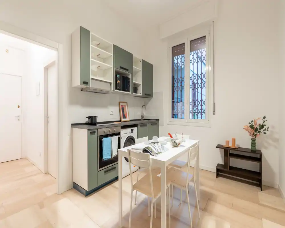 Cucina moderna e luminosa con elettrodomestici integrati e piccolo tavolo da pranzo; toni neutri e linee pulite con un allestimento del tavolo accogliente, perfetta per spazi urbani compatti.